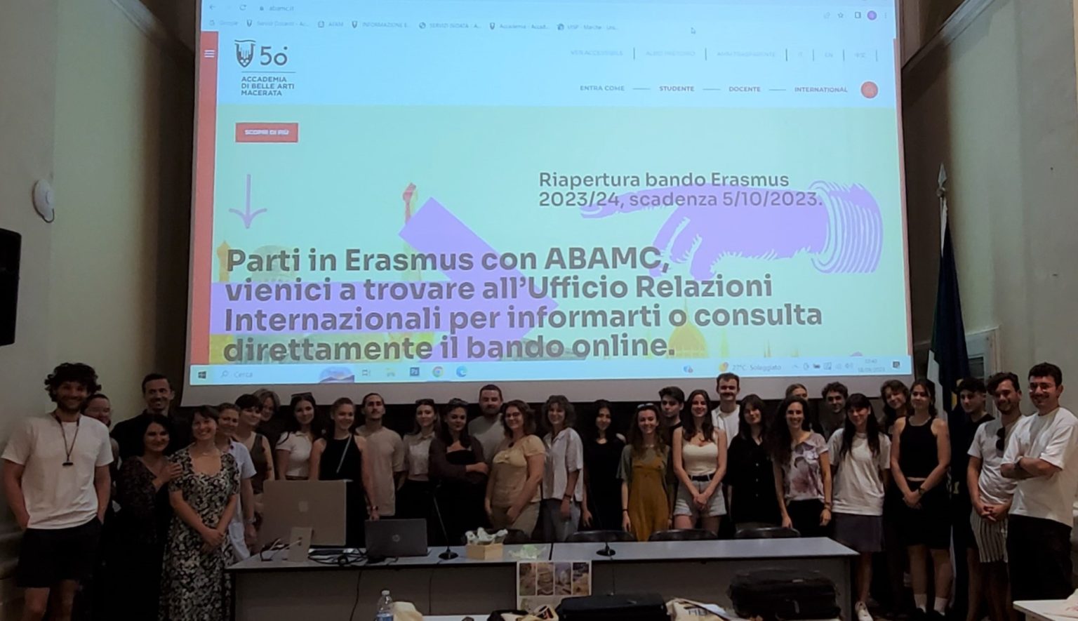 Zdjęcie grupowe uczestników wykładu. Duża grupa ludzi stoi pod ekranem na sali wykładowej